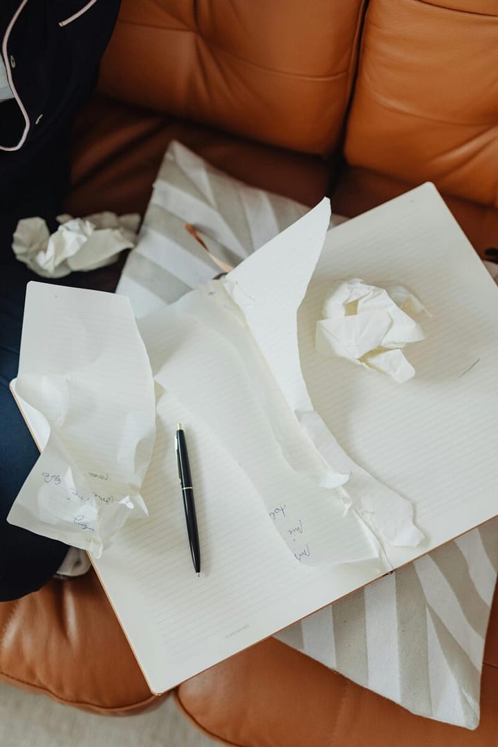 Torn papers and a pen scattered on an open notebook in a cozy indoor setting.